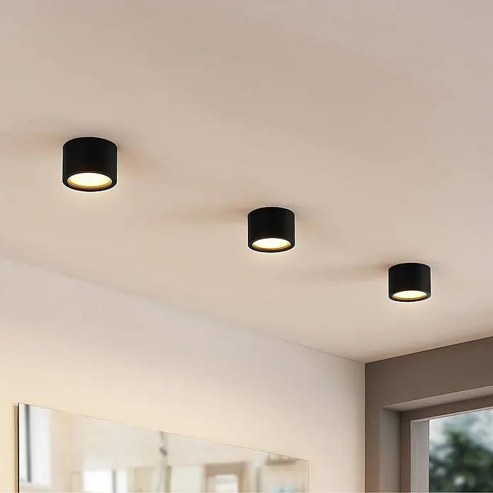 Arcchio Deckenstrahler Nieva - L x B x H: 10 x 10 x 6,5 cm, schwarz, schwarz, 2GX53 - Drei schwarze zylindrische Deckenstrahler beleuchten einen Raum, an einer hellen Decke montiert.