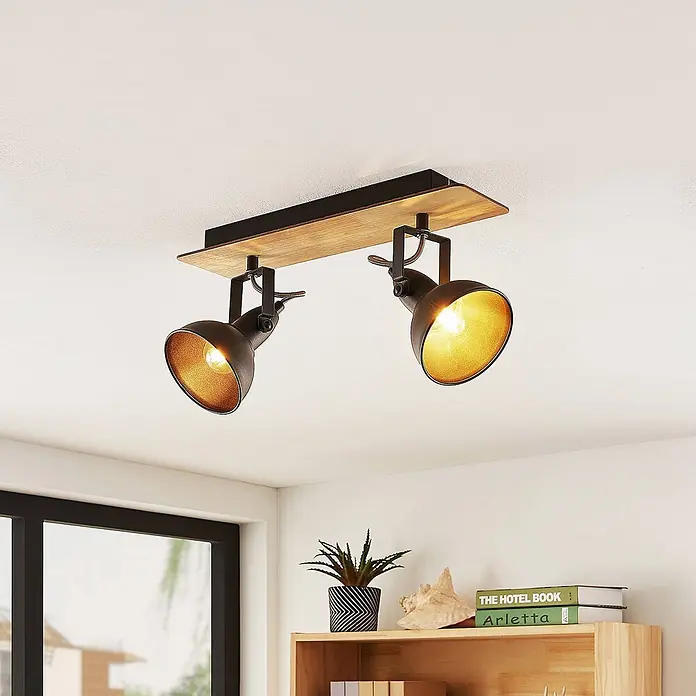 Lindby Deckenstrahler Aylis - Holz dunkel, schwarz, E14 - Industrielle Deckenleuchte mit zwei schwarzen Metall-Spots, goldenen Innenseiten und Holzsockel, an der Decke montiert.