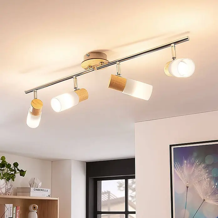 Lindby Deckenstrahler Christoph - Holz hell, E14 - Moderne Deckenleuchte mit vier verstellbaren Strahlern aus Naturholz, Chrom und weißem Milchglas, die einen Raum beleuchten.