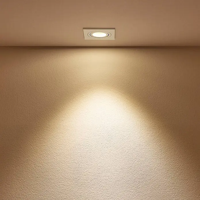 Arcchio Deckenstrahler Sophia - weiß / opal, GU10 - Quadratischer, weißer Einbaustrahler beleuchtet eine strukturierte Wand mit warmem Licht.