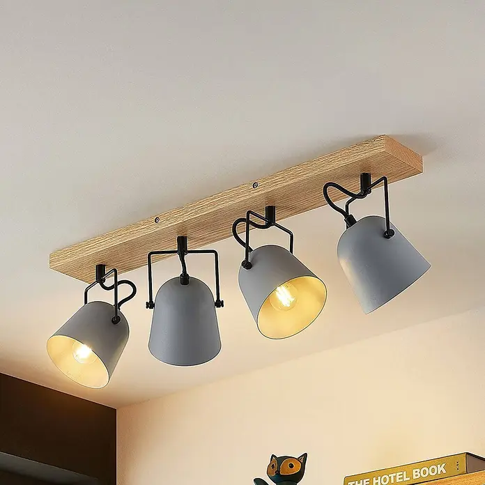 Lindby Deckenstrahler Adalin - Holz hell, alu / grau / zink, E14 - Vier graue Metall-Strahler an einem Holz-Balken als Deckenleuchte, zwei Lampen strahlen warmes Licht ab.