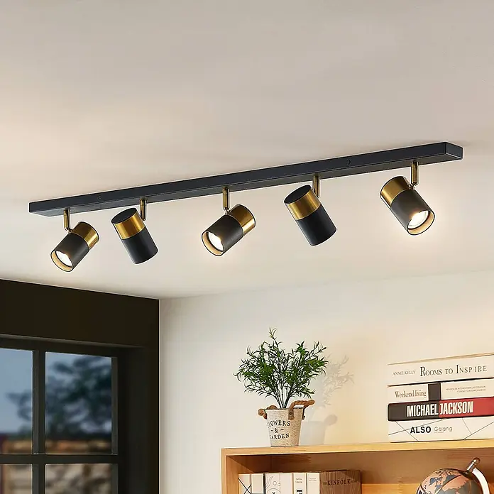 Arcchio Deckenstrahler Evaro - schwarz, schwarz, GU10 - Fünf schwarz-goldene Deckenstrahler an einer Leiste beleuchten einen modernen Wohnraum.