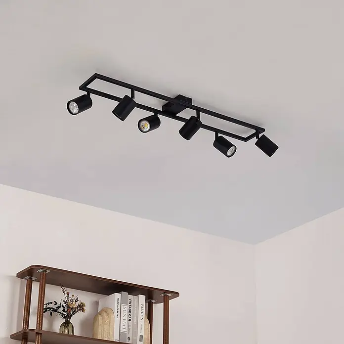 Lindby Deckenstrahler Bravius - L x B x H: 80 x 12 x 15 cm, schwarz, schwarz, GU10 - Schwarze Deckenleuchte mit sechs verstellbaren Strahlern über einem Holzregal, die den Raum beleuchten.