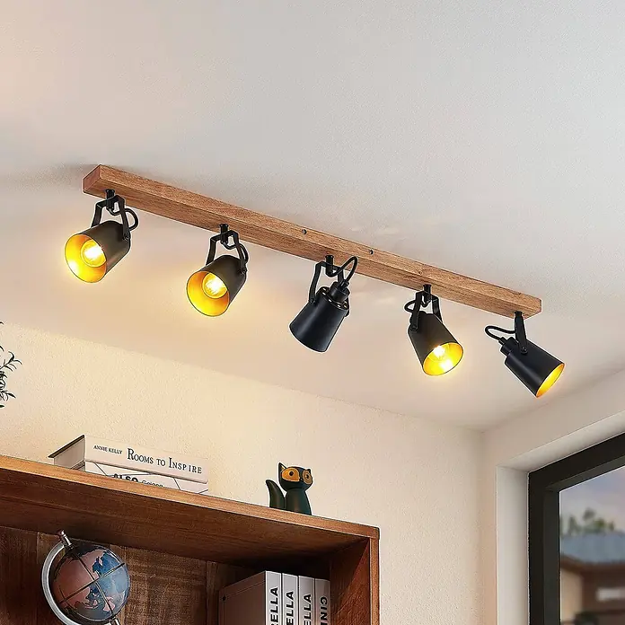 Lindby Deckenstrahler Kimban - L x B x H: 106,5 x 8,3 x 15,8 cm, Holz dunkel, schwarz, E14 - Hölzerne Schienenleuchte mit fünf schwarzen Strahlern, einige davon warm leuchtend, an einer Decke montiert.