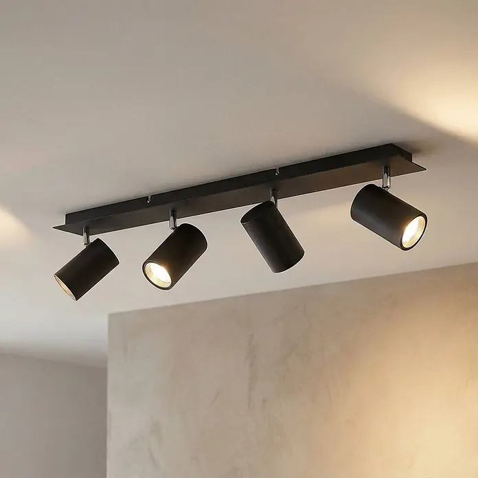 Lindby Deckenstrahler Joffrey - schwarz, schwarz, GU10 - Schwarze Deckenleuchte mit vier verstellbaren zylindrischen Strahlern, montiert und beleuchtet eine strukturierte Wand.
