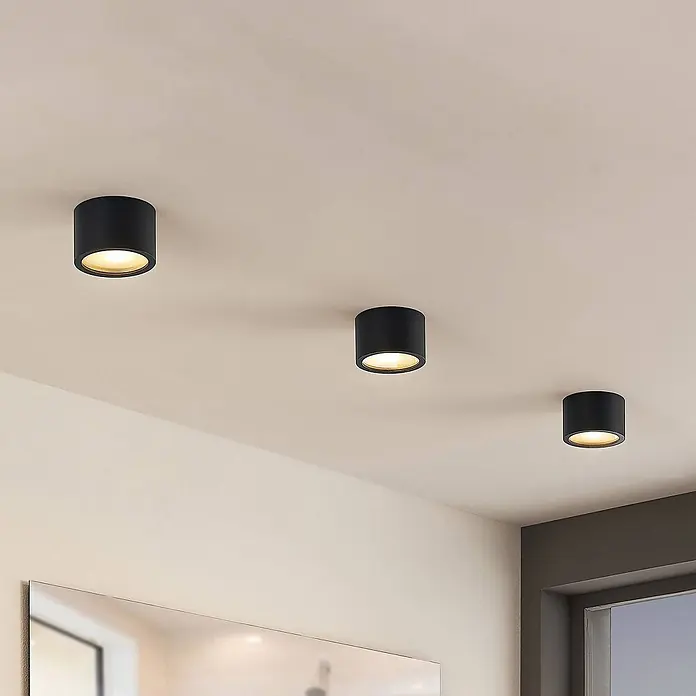 Arcchio Deckenstrahler Nieva - L x B x H: 10 x 10 x 6,5 cm, schwarz, schwarz, G9 - Schwarze zylindrische Deckenaufbaustrahler an einer hellen Decke, die warmes Licht abstrahlen.