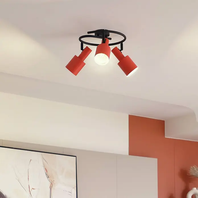 Lindby Deckenstrahler Ovelia - gelb / orange, E27 - Drei rote zylindrische Strahler an einer schwarzen runden Deckenhalterung beleuchten einen modernen Raum. Die Leuchten sind nach unten gerichtet.