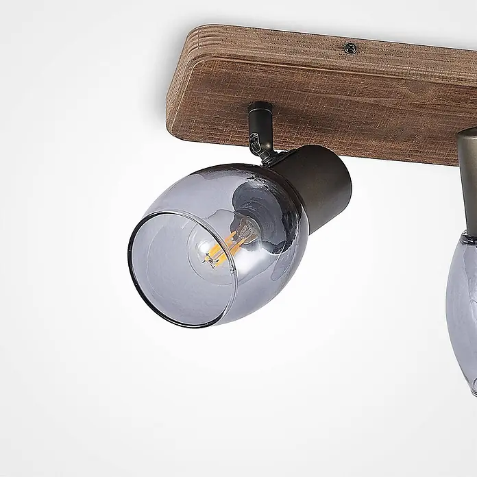 Lindby Deckenstrahler Ineska - Holz dunkel, E14 - Deckenstrahler mit braunem Holzsockel und rauchgrauem Glasschirm, zeigt eine LED-Filamentlampe.