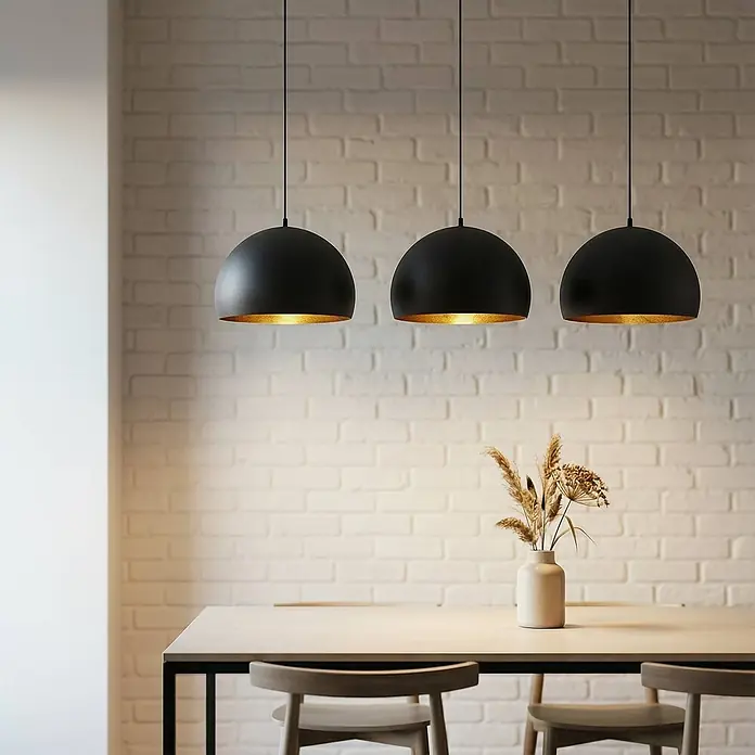 Lindby Pendelleuchte Tarjei - schwarz, Schwarz, gold, E27 - Drei schwarze Pendelleuchten mit goldenem Interieur beleuchten einen Esstisch.