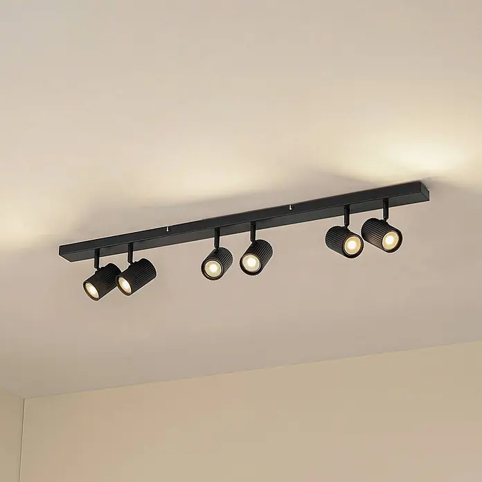 Lindby Deckenstrahler Kardis - L x B x H: 100 x 6 x 16 cm, alu / grau / zink, alu / grau / zink, GU10 - Schwarze Deckenleuchte mit sechs zylindrischen Strahlern, teilweise beleuchtet, an einer hellen Decke montiert.