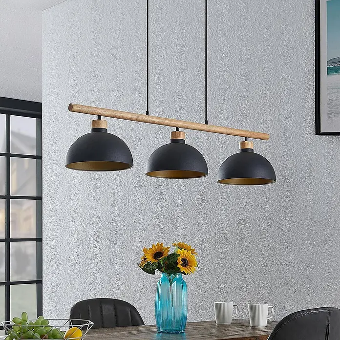 Lindby Pendelleuchte Tirzana - L x B x H: 100 x 25 x 12,5 cm, schwarz, Schwarz, gold, holz hell, E27 - Drei-flammige Pendelleuchte mit schwarzen Kuppelschirmen und Holzbalken über einem Esstisch.