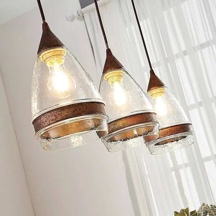 Lindby Pendelleuchte Millina - L x B x H: 70,4 x 15,6 x 25,8 cm, klar / transparent, rostbraun, klar, E27 - Drei rustikale Pendelleuchten mit klaren, strukturierten Glasschirmen und Bronzeakzenten erhellen einen Raum.