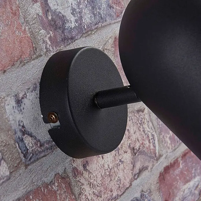 Lindby Deckenstrahler Morik - L x B x H: 19 x 10 x 12 cm, schwarz, schwarz, E14 - Schwarze Metall-Wandleuchte mit rundem Sockel, an einer Ziegelwand montiert.