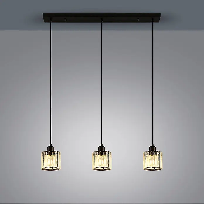 Lindby Pendelleuchte Vella - L x B x H: 83 x 13 x 12,3 cm, klar / transparent, mattSchwarz, transparent, E27 - Drei Pendelleuchten mit schwarzer Rechteck-Deckenplatte, schwarzen Kabeln und zylindrischen Kristallschirmen mit beleuchteten Glühbirnen.