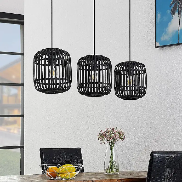 Lindby Pendelleuchte Canyana - schwarz, Schwarz, E27 - Drei schwarze Rattan-Pendelleuchten mit Käfigdesign und sichtbaren Glühbirnen hängen über einem Esstisch.