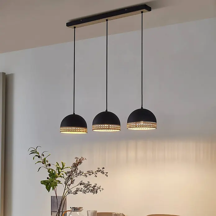 Lindby Pendelleuchte Lonnaris - L x B x H: 70 x 20 x 21 cm, schwarz, Schwarz, rattan natur, E14 - Dreiflammige Pendelleuchte mit schwarzen Kuppelschirmen und Rattan-Akzenten, die einen Tisch beleuchtet.