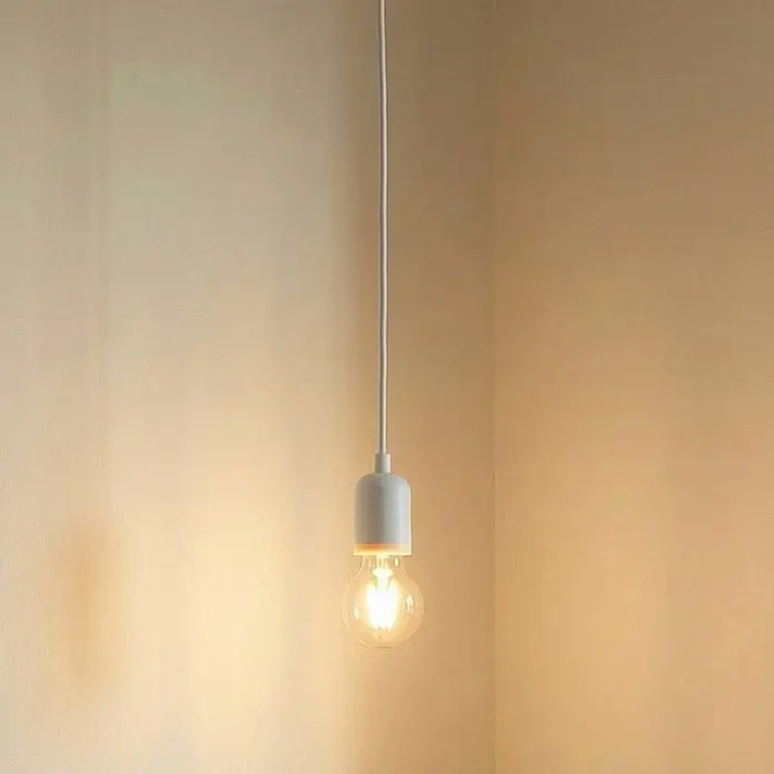 Lindby Pendelleuchte Hattie - weiß / opal, weiß, E27 - Eine leuchtende Glühbirne mit weißer Fassung und Kabel hängt in einer Zimmerecke und spendet warmes Licht.
