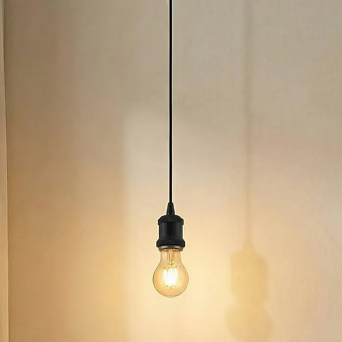 Lindby Pendelleuchte Hattie - L x B x H: 5 x 5 x 6,5 cm, schwarz, Schwarz, E27 - Eine leuchtende Glühbirne mit schwarzer Fassung und Kabel, die eine Wand beleuchtet.