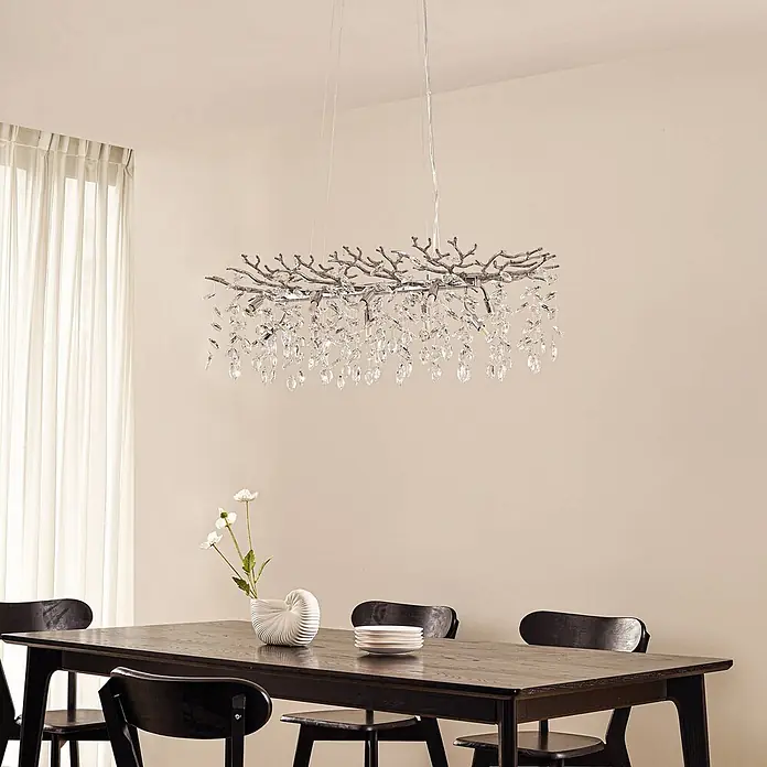 Lucande Pendelleuchte Bellora - L x B x H: 101 x 45 x 32 cm, klar / transparent, chrom, transparent, G9 - Kronleuchter aus Chrom mit Ast-Design und Kristalltropfen über einem dunklen Esstisch.