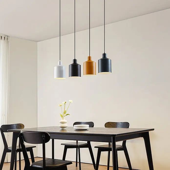 Lindby Pendelleuchte Tirane - L x B x H: 94 x 16 x 13 cm, Multicolour, Schwarz, weiß, Grün, gelb, E27 - Verschiedene zylindrische Pendelleuchten beleuchten einen Esstisch mit Stühlen.