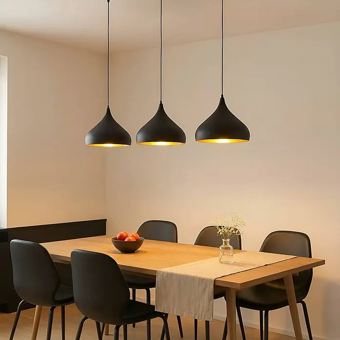 Lindby Pendelleuchte Elamira - L x B x H: 133 x 31 x 150 cm, schwarz, Schwarz, gold, E27 - Drei schwarze Pendelleuchten mit goldenem Interieur hängen über einem Holzesstisch.