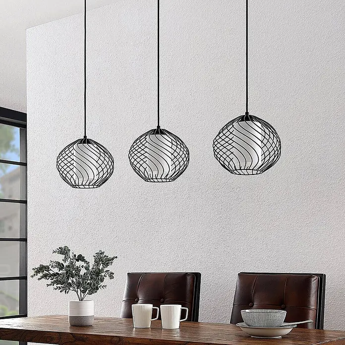 Lindby Pendelleuchte Cedrice - L x B x H: 108 x 25 x 21 cm, schwarz, Schwarz, weiß, E27 - Drei schwarze Metall-Spiralpendelleuchten mit weißen Innenschirmen hängen über einem Holztisch.