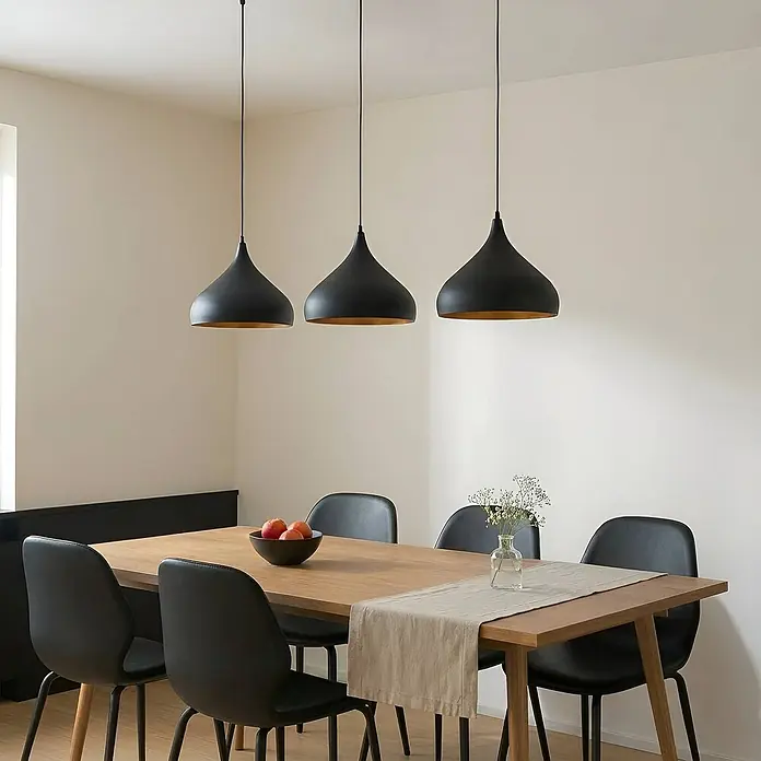 Lindby Pendelleuchte Elamira - L x B x H: 133 x 31 x 150 cm, schwarz, Schwarz, gold, E27 - Drei schwarze Pendelleuchten mit goldener Innenseite hängen über einem Holztisch mit schwarzen Stühlen.