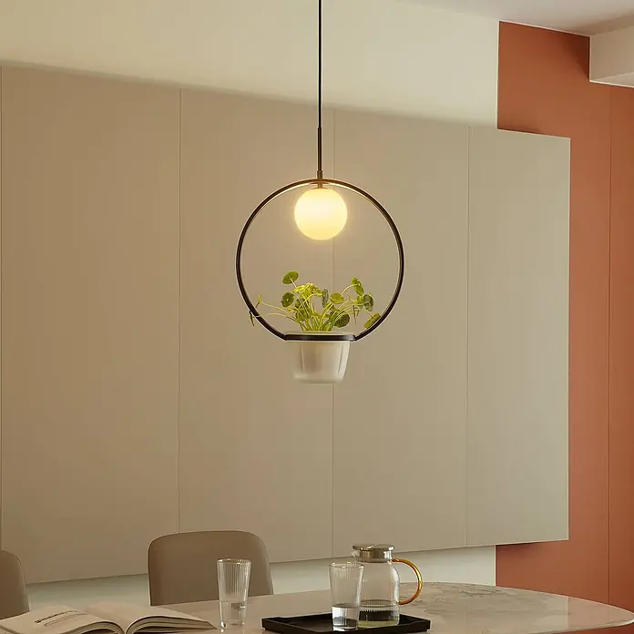 Lindby Pendelleuchte Orna - L x B x H: 40 x 17,2 x 12,4 cm, Schwarz, opal, G9 - Moderne schwarze runde Pendelleuchte mit integriertem mattiertem Pflanzgefäß und Grünpflanze über einem Tisch.