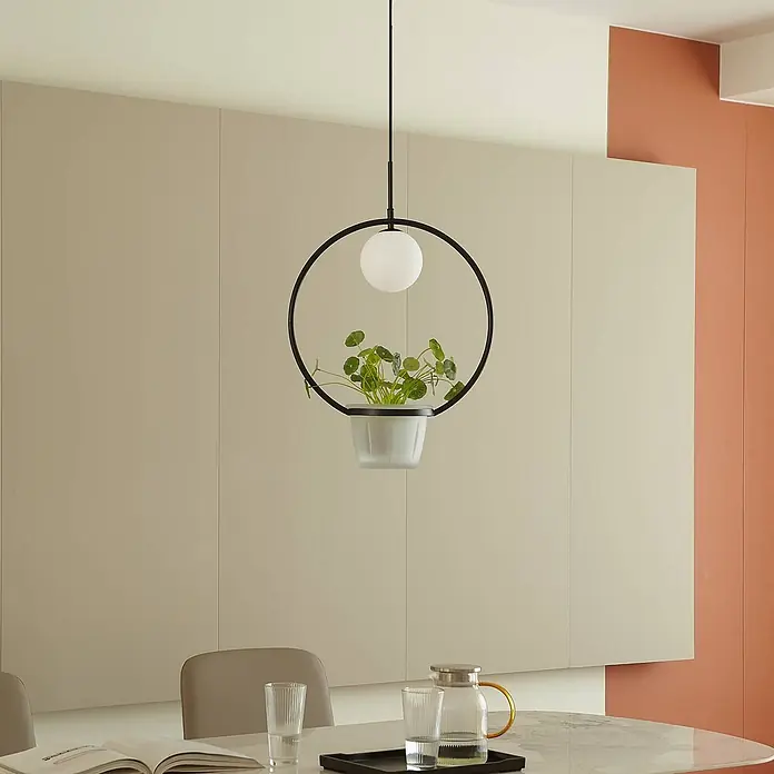 Lindby Pendelleuchte Orna - L x B x H: 40 x 17,2 x 12,4 cm, Schwarz, opal, G9 - Schwarze kreisförmige Pendelleuchte mit weißer Kugellampe und integriertem Pflanztopf, über einem Tisch hängend.