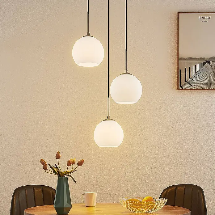 Lindby Pendelleuchte Jurian - L x B x H: 32 x 32 x 17,5 cm, weiß / opal, opal, nickel, E27 - Drei kugelförmige Pendelleuchten aus weißem Glas mit Messingakzenten über einem Esstisch.