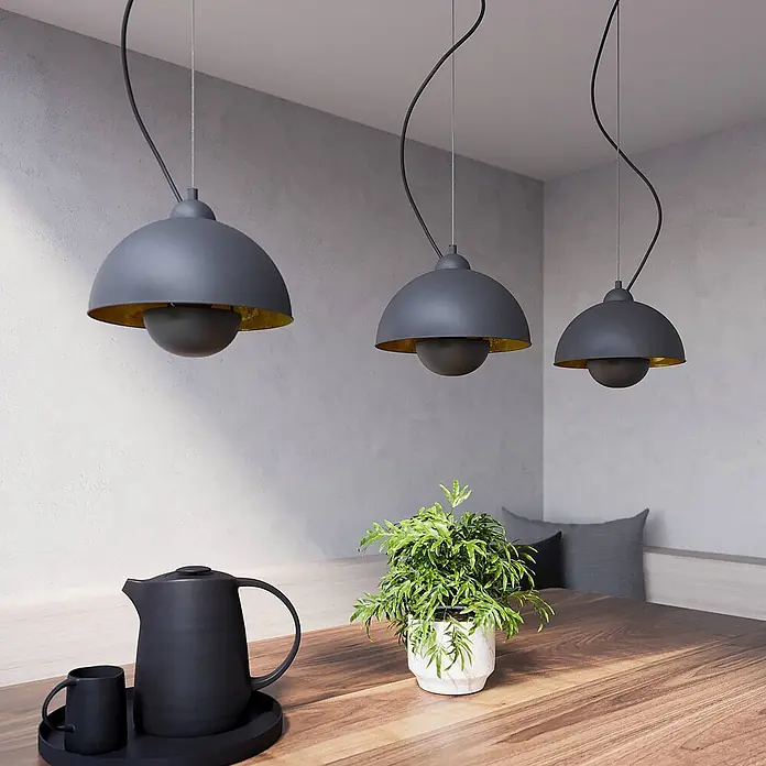 Lindby Pendelleuchte Gretja - L x B x H: 120,5 x 25 x 150 cm, schwarz, Schwarz, gold, E27 - Drei graue Pendelleuchten mit goldener Innenseite hängen über einem Holztisch in einem modernen Interieur.