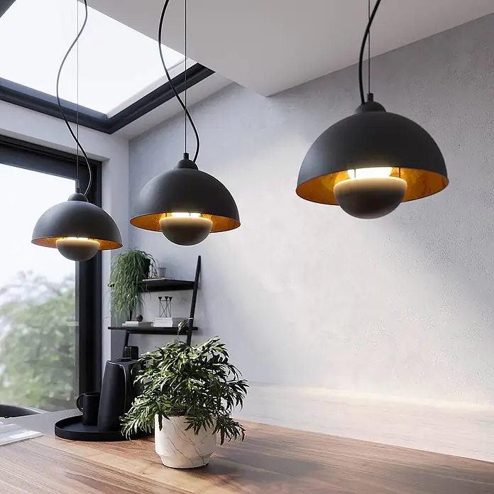 Lindby Pendelleuchte Gretja - L x B x H: 120,5 x 25 x 150 cm, schwarz, Schwarz, gold, E27 - Drei moderne schwarze Pendelleuchten mit goldenen Innenseiten über einem Holztisch in einem Raum.