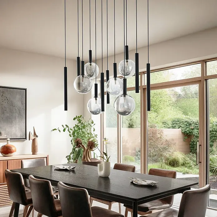 Lucande Pendelleuchte Lumavia - L x B x H: 93 x 53 x 30 cm, schwarz, Schwarz, rauchgrau, G9 - Eine mehrflammige Pendelleuchte mit schwarzen Zylindern und klaren Glaskugeln hängt über einem dunklen Esstisch in einem modernen Esszimmer.