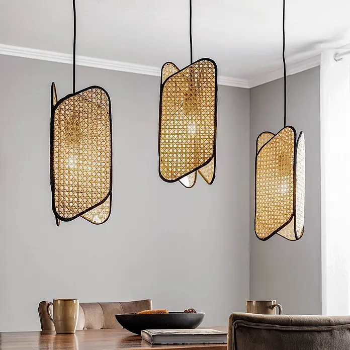 Lucande Pendelleuchte Bassiola - L x B x H: 100 x 19 x 37 cm, Holz hell, Schwarz, Holz hell, E27 - Drei Hängelampen mit Rattan-Schirmen und schwarzen Rahmen hängen über einem Holztisch.