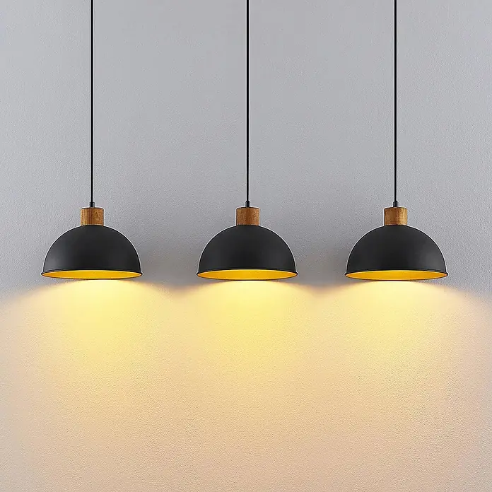 Lindby Pendelleuchte Flurin - schwarz, sandSchwarz, gold, holz, E27 - Drei schwarze, kuppelförmige Pendelleuchten mit goldener Innenseite und Holzdetails, die warmes Licht abstrahlen.
