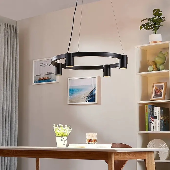 Arcchio Pendelleuchte Brinja - schwarz, Schwarz, GU10 - Eine schwarze kreisförmige Pendelleuchte mit mehreren Strahlern hängt über einem hellen Holztisch.