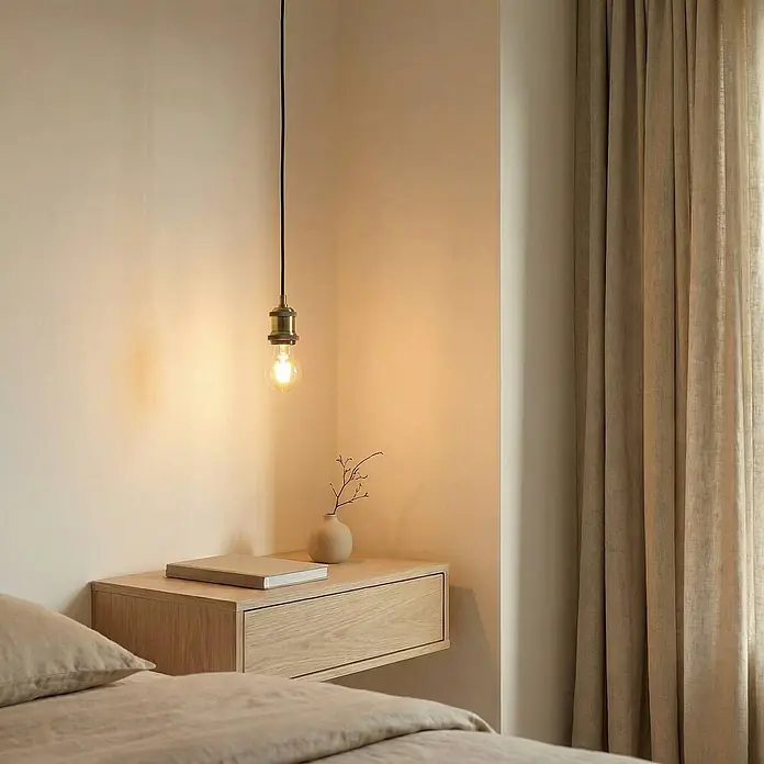 Lindby Pendelleuchte Hattie - messing / gold, messing, E27 - Ein minimalistisches Schlafzimmer mit Messing-Pendelleuchte und Glühbirne über einem schwebenden Nachttisch aus hellem Holz neben einem Bett.