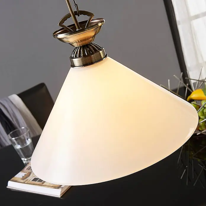 Lindby Pendelleuchte Otis - L x B x H: 30 x 30 x 15 cm, opalweiß glänzend, altmessing, E27 - Pendelleuchte in Messing-Optik mit weißem, konischem Glasschirm, beleuchtet über einem Tisch hängend.