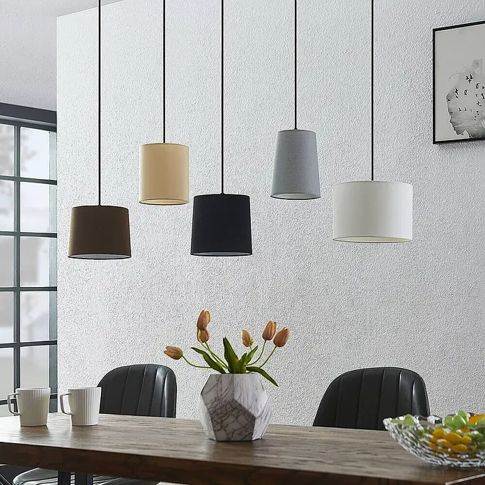 Lindby Pendelleuchte Amilia - Multicolour, Holz natur, Schwarz, grau, beige, braun, weiß, E27 - Fünf Hängelampen aus Stoff in Braun, Beige, Schwarz, Grau und Weiß hängen über einem Holztisch.