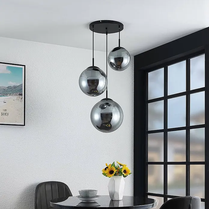 Lindby Pendelleuchte Teeja - L x B x H: 51,5 x 51,5 x 30 cm, alu / grau / zink, rauchgrau, Schwarz, E27 - Dreiflammige Pendelleuchte mit rauchgrauen Glaskugeln und schwarzer Deckenplatte über einem Esstisch.