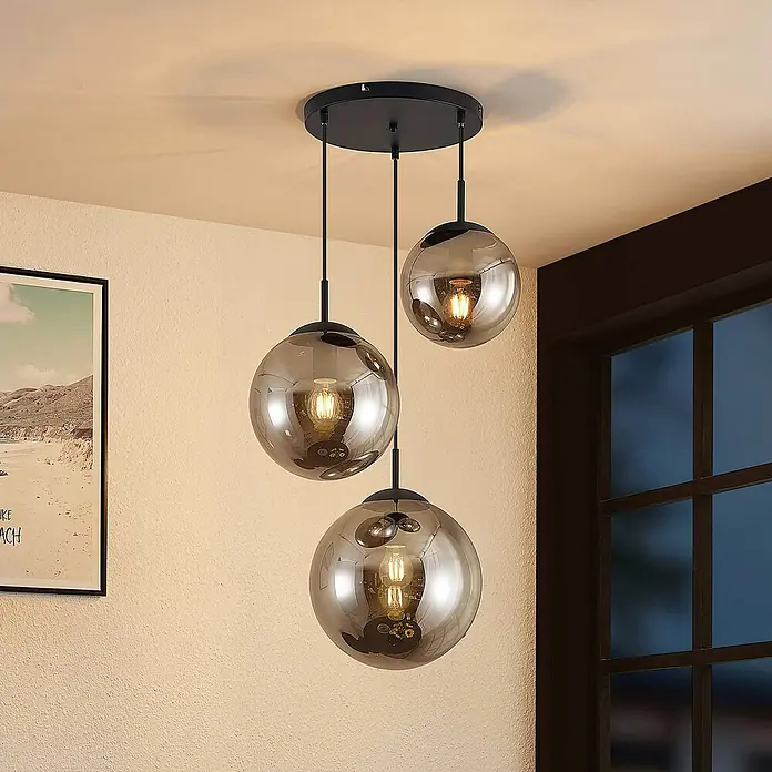Lindby Pendelleuchte Teeja - L x B x H: 51,5 x 51,5 x 30 cm, alu / grau / zink, rauchgrau, Schwarz, E27 - Dreiflammige Pendelleuchte mit Rauchglas-Kugeln und schwarzer Deckenhalterung, die einen Raum beleuchtet.