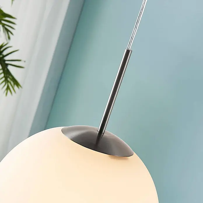 Lindby Pendelleuchte Marike - L x B x H: 30 x 30 x 150 cm, weiß / opal, weiß, nickel satiniert, E27 - Kugelförmige Pendelleuchte mit opalem weißem Glasschirm und gebürsteter Metallaufhängung, vor einer hellblauen Wand.