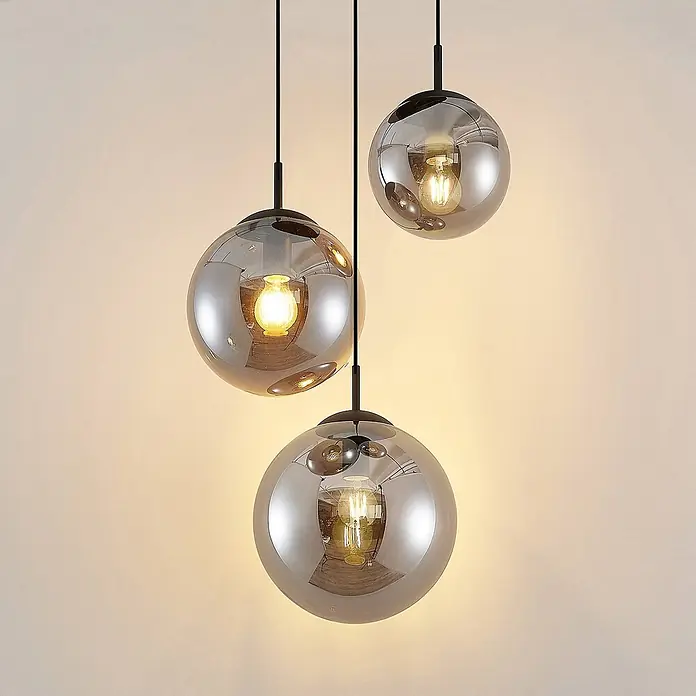 Lindby Pendelleuchte Teeja - L x B x H: 51,5 x 51,5 x 30 cm, alu / grau / zink, rauchgrau, Schwarz, E27 - Drei Pendelleuchten mit kugelförmigen, rauchfarbenen Glasschirmen und leuchtenden Glühbirnen.