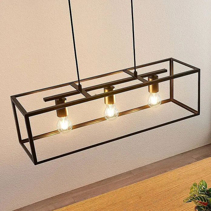 Lindby Pendelleuchte Emily - L x B x H: 72 x 20 x 20 cm, schwarz, Schwarz matt, E27 - Rechteckige schwarze Pendelleuchte aus Metall mit Messingdetails und drei Glühbirnen, hängt über einem Holztisch.