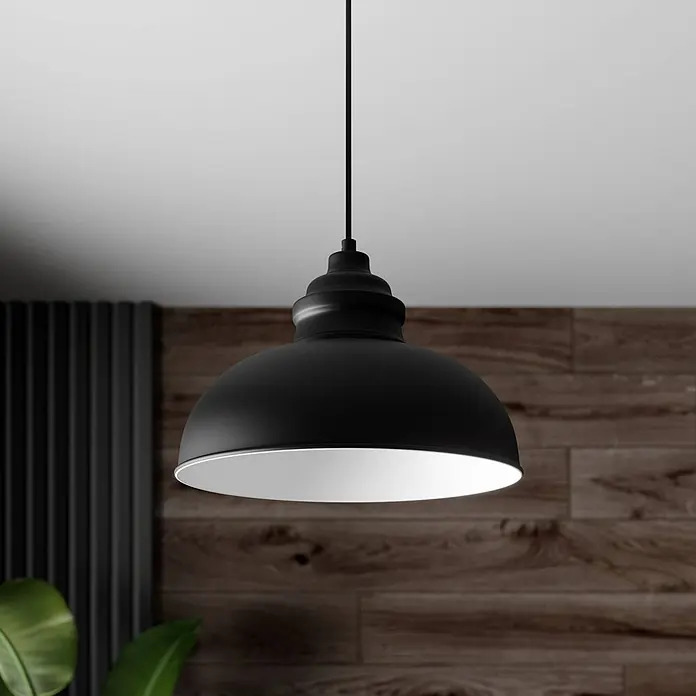 Lindby Pendelleuchte in schwarz matt, weiß, Hängelampe -  - Eine mattschwarze Pendelleuchte mit weißer Innenseite hängt von der Decke, beleuchtet vor einer rustikalen Holzwand und grünem Laub.