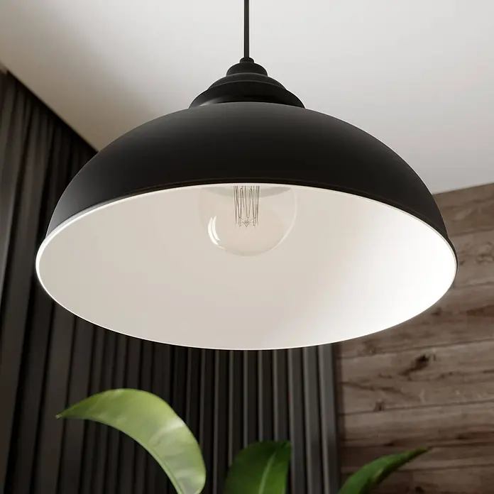 Lindby Pendelleuchte in schwarz matt, weiß, Hängelampe -  - Schwarze Metall-Pendelleuchte mit weißer Innenseite und sichtbarer Glühbirne, in einem Raum mit Holzwand und Pflanze hängend.