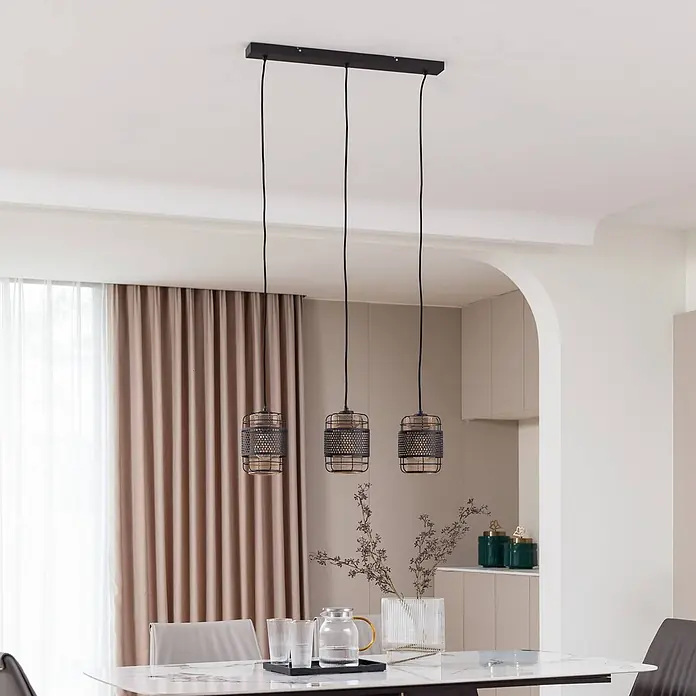 Lindby Pendelleuchte Eudoria - schwarz, Schwarz, gold, E27 - Drei schwarze Gitter-Pendelleuchten mit beigen Innenschirmen hängen über einem Esstisch.