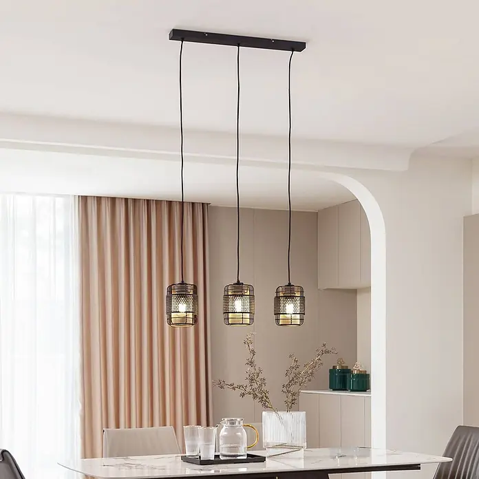 Lindby Pendelleuchte Eudoria - schwarz, Schwarz, gold, E27 - Drei schwarze Pendelleuchten aus Metallgeflecht hängen über einem Esstisch in modernem Interieur.