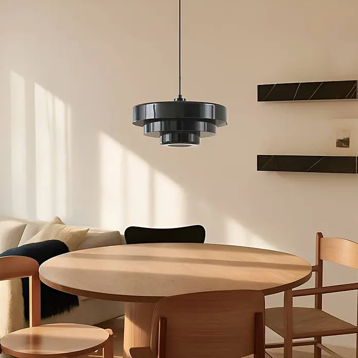 Lindby Pendelleuchte Tivra - schwarz, Schwarz, E27 - Eine schwarze, gestufte Pendelleuchte hängt über einem runden Holztisch und beleuchtet den Essbereich.