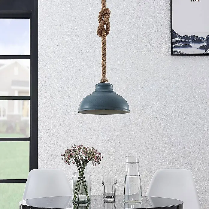 Lindby Pendelleuchte Chaby - alu / grau / zink, beton, E27 - Eine blaue Pendelleuchte mit Seilaufhängung hängt über einem modernen Esstisch.